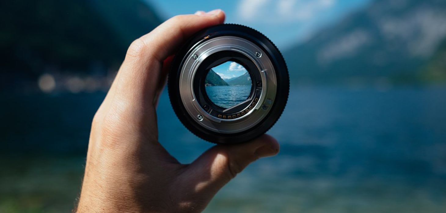 hand with camera lense and scenery in background